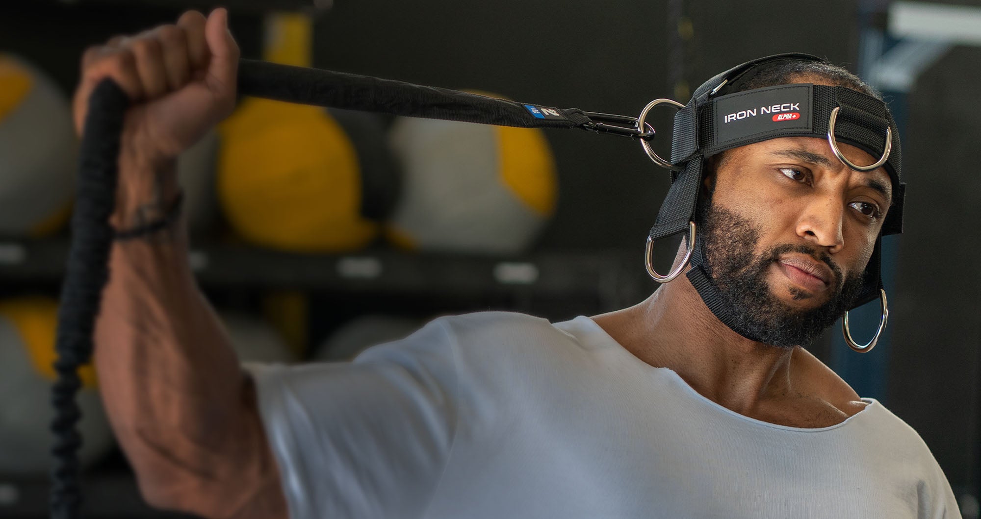 Man wearing an 'Iron Neck' harness in a gym setting